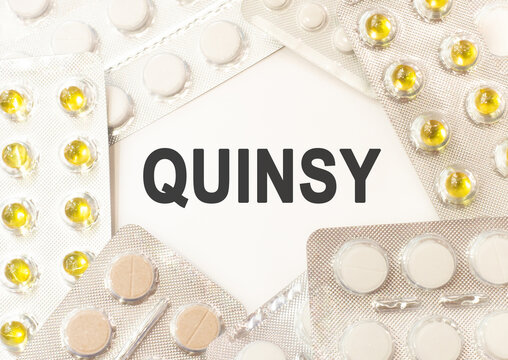 Text quinsy on white background. There are various pills and vitamins around. Medicine concept