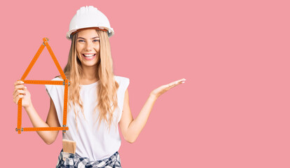 Beautiful caucasian woman with blonde hair wearing architect hardhat and holding tools celebrating victory with happy smile and winner expression with raised hands
