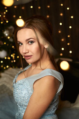
Beautiful woman in a blue evening dress on the background of a Christmas tree and garlands. Holiday concept, new year, christmas, sale and discounts.