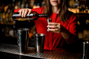 Close-up of bartender's hand holding bottle and pours liquid into metal jigger