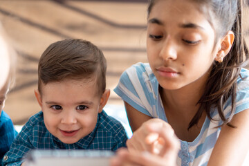 friendship, childhood, technology concepts - 2 young children baby of different nationalities Persian and Slavic appearance watch cartoon on smartphone on bed. kids preschool speak by video conference