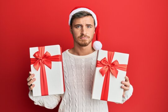 Handsome caucasian man wearing christmas hat and holding gifts depressed and worry for distress, crying angry and afraid. sad expression.