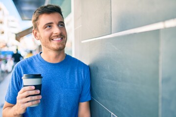 Young caucasian man using smartphone and drinking take away coffee at the city.