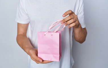 Fototapeta na wymiar man in a t-shirt with a pink gift bag on a light background