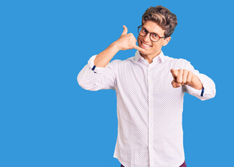 Naklejka premium Young handsome man wearing business clothes and glasses smiling doing talking on the telephone gesture and pointing to you. call me.