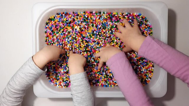 Two girls playing with perler beads in a box using hands top view