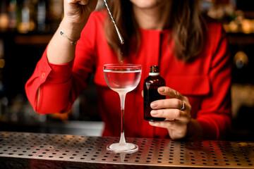 glass with liquid stand on bar and bartender adds ingredient into it