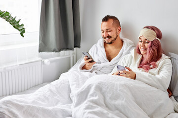 Obraz na płótnie Canvas caucasian couple using smartphone lying on bed together, checking social networks news in the morning, relax time