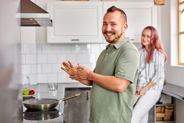 Fototapeta na wymiar cheerful couple cooking in the kitchen, young man and woman laugh, looking at camera. focus on male