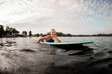 Fototapeta na wymiar happy young blonde woman lying on surf board and floating on water
