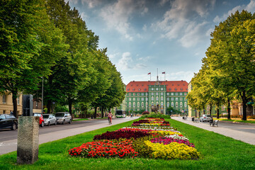 Colourful flowerbeds and tress on avenue of Pope John Paul II with green buildings of Szczecin City Council in the background