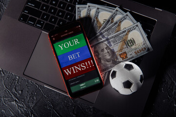 Smartphone with gambling mobile application, ball and money banknotes on a keyboard. Sport and betting concept.