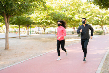 Attractive hispanic couple wearing face masks is exercising outdoors