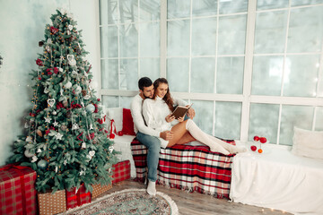 young couple in love sitting on windowsill and reading book in christmas home interior