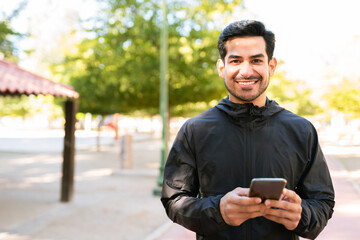 Sporty man making eye contact and smiling with his smartphone