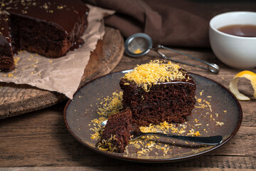 A broken piece of chocolate cake with lemon zest on a wooden background. Side view. The concept of cooking.