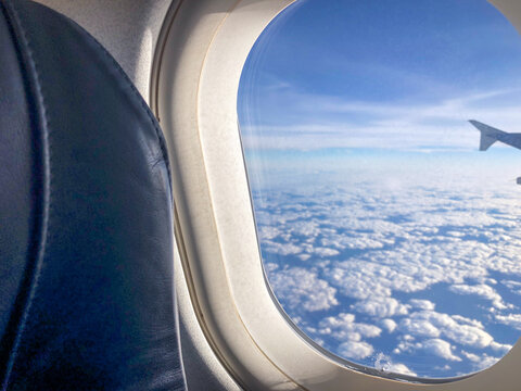 Looking Out Airplane Window, Airplane Wing And Clouds. View Out Of Airplane Window Above The Atlantic Ocean On Bright Sunny Day. 