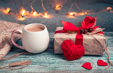 A Cup of coffee, a gift and a heart on a festive background with a garland. Side view with space for copying. Concept February 14.