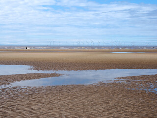 the beach at blundell sands in sefton, near southport with pools on the beach the beach and the wind turbines at burbo bank visible in the distance