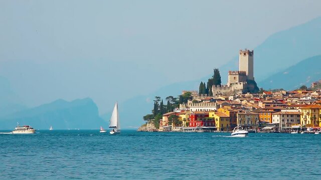 Malcesine, Lake Garda, Italy. Picturesque landscape of the lake with ancient small village town on the banks among the Alps Mountains. Ships and jachts on the water