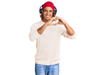 Young hispanic man listening to music using headphones smiling in love doing heart symbol shape with hands. romantic concept.