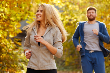 couple running at autumn forest trail, young caucasian fit man and woman warming up outdoors, enjoy running jogging