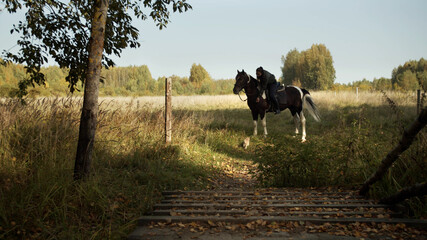 Scenic shot, rural landscape on a ranch with a young girl in the saddle of a classic american...