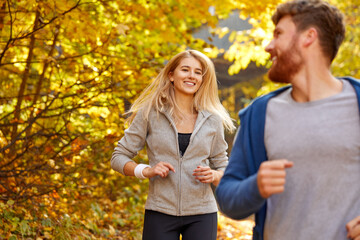 couple run together in the autumn forest, athletic sportive man and woman in sportswear enjoy jogging on fresh air, at sunny day