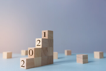 The numbers 2021 are on wooden blocks shaped as stairs with blue background. New year 2021 concept. Selective focus with depth of field.