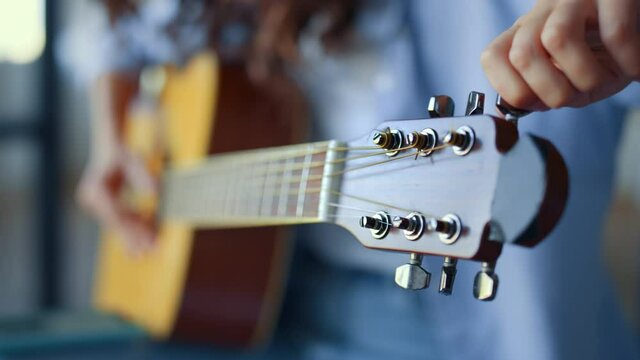 Girl hands tuning guitar. Young woman checking pegs of acoustic guitar