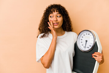 Young african american afro woman holding a scale is saying a secret hot braking news and looking...