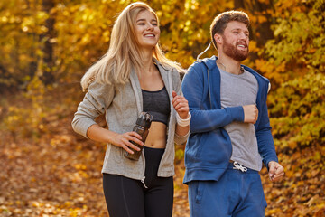 fit couple training jogging ay sunny autumn day outdoors, athletic caucasian man and woman. active couple jogging