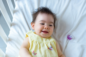 Bebe pequeño en cuna blanca con vestido amarillo