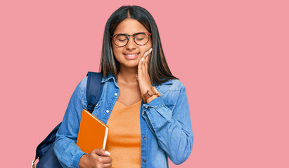 Young latin girl wearing student backpack and holding books touching mouth with hand with painful expression because of toothache or dental illness on teeth. dentist concept.