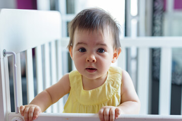 Bebe pequeño en cuna blanca con vestido amarillo