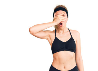 Fototapeta premium Young beautiful blonde woman wearing sportswear peeking in shock covering face and eyes with hand, looking through fingers with embarrassed expression.