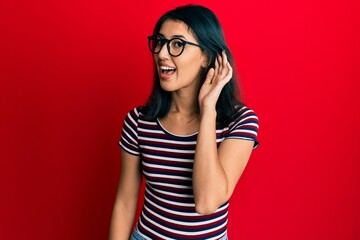 Beautiful asian young woman wearing casual clothes and glasses smiling with hand over ear listening and hearing to rumor or gossip. deafness concept.