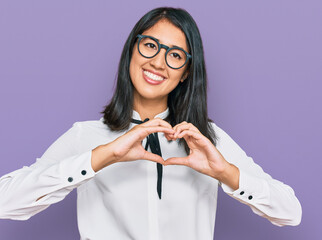 Beautiful asian young woman wearing business shirt and glasses smiling in love showing heart symbol and shape with hands. romantic concept.