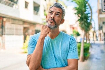 Middle age grey-haired man wearing casual clothes at street of city serious face thinking about question with hand on chin, thoughtful about confusing idea