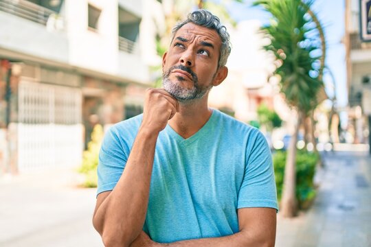 Middle age grey-haired man wearing casual clothes at street of city serious face thinking about question with hand on chin, thoughtful about confusing idea