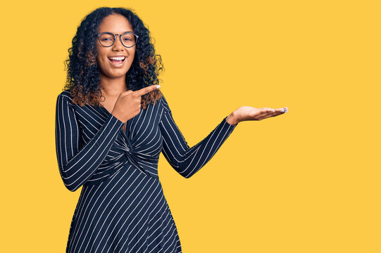 Young african american woman wearing casual clothes and glasses amazed and smiling to the camera while presenting with hand and pointing with finger.