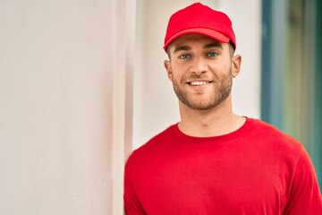 Young caucasian deliveryman smiling happy standing at the city.