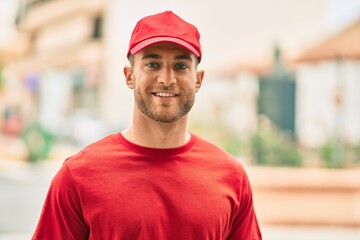 Young caucasian deliveryman smiling happy standing at the city.