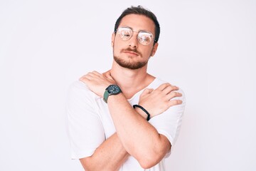 Young handsome man wearing casual clothes and glasses hugging oneself happy and positive, smiling...