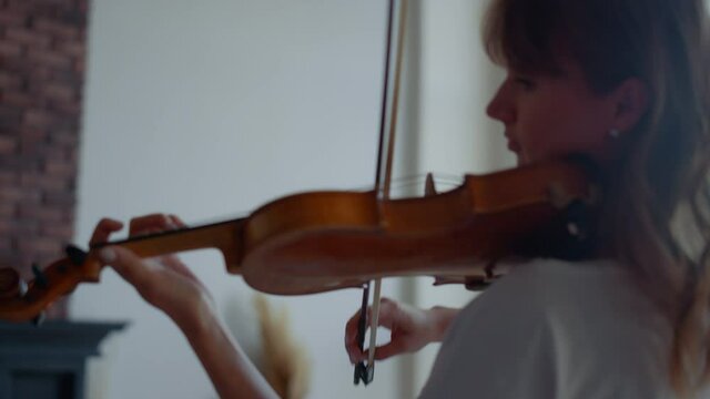 Woman playing musical composition on violin. Attractive girl using violin bow