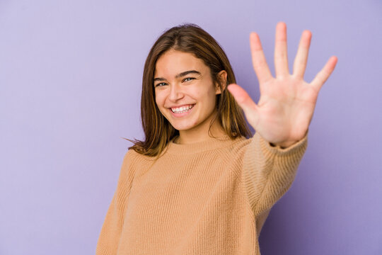 Young skinny caucasian girl teenager on purple background smiling cheerful showing number five with fingers.