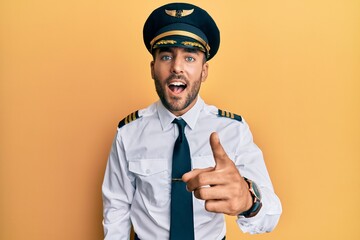 Handsome hispanic man wearing airplane pilot uniform pointing displeased and frustrated to the camera, angry and furious with you