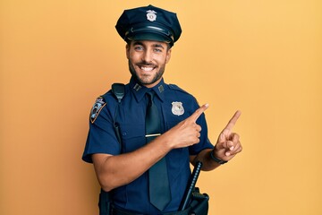 Handsome hispanic man wearing police uniform smiling and looking at the camera pointing with two...