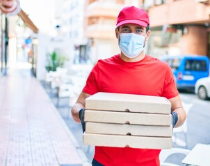 Fototapeta na wymiar Young delivery man wearing uniform and coronavirus protection medical mask. Holding deliver pizza boxes at town street.
