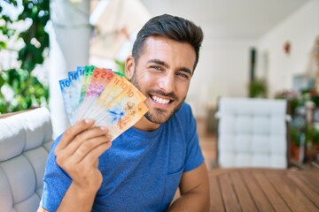 Young hispanic man smiling happy holding swiss franc banknotes at the terrace.